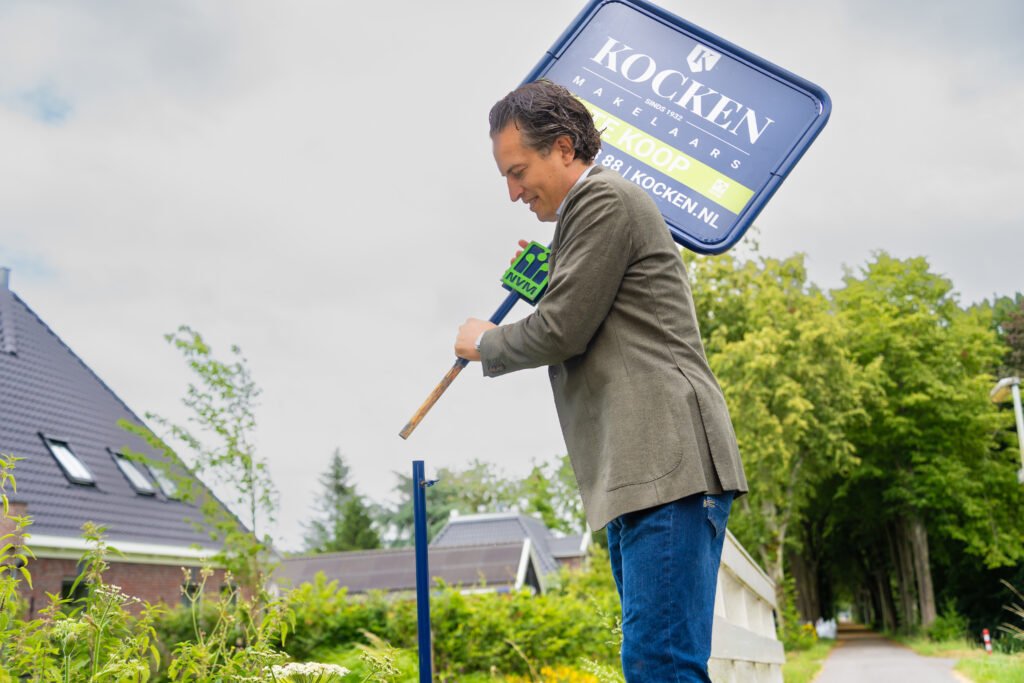 Makelaar van Kocken Makelaars plaatst een te koop bord in de tuin van een woning in Purmerend
