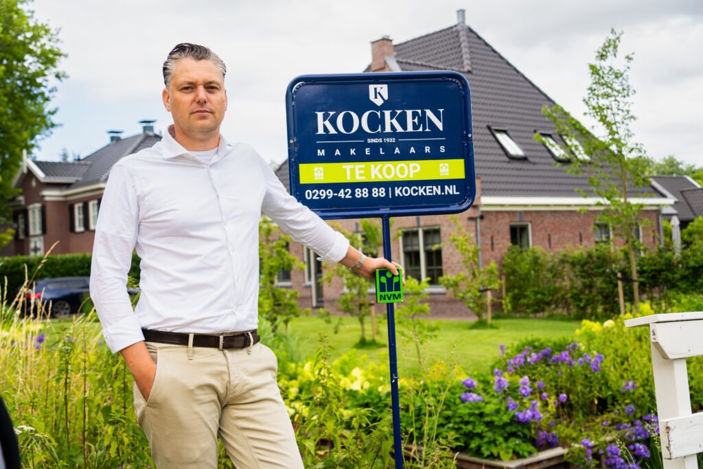 Makelaar van Kocken Makelaars naast een te koop bord in de tuin van een vrijstaande woning in Purmerend